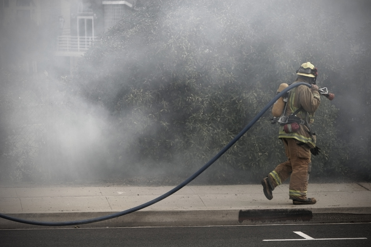Profile view of firefighter walking down a smokey street carrying a hose